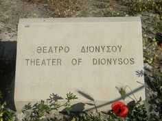 there is a sign on the ground that says theater of donymosos and two red flowers