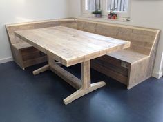 a wooden table with benches underneath it in front of a window and potted plants