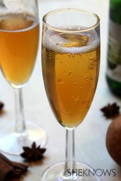 two wine glasses filled with liquid next to an apple and cinnamon peel on a table