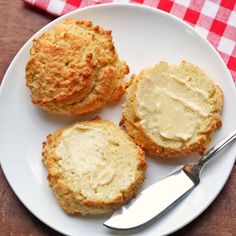 three biscuits on a white plate with butter and a knife next to it, sitting on a red checkered tablecloth