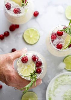 two people holding glasses filled with drinks and garnished with raspberries