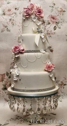 a three tiered wedding cake with pink flowers and pearls on the top is decorated in white frosting