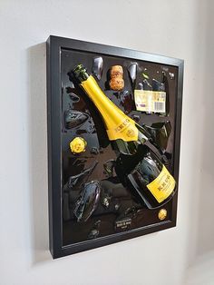 a bottle of wine and some other items on a black framed wall hanging in a white walled room