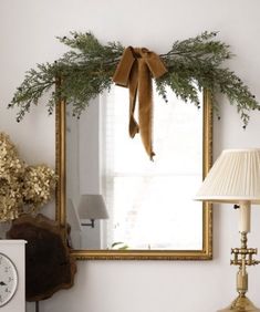 a mirror hanging on the wall above a table with a lamp and vase in front of it