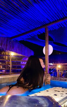 a woman sitting in the middle of a pool with blue lights on her face and long black hair