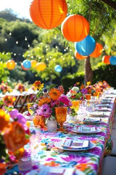 a long table is set with colorful paper lanterns hanging from the ceiling and flowers in vases