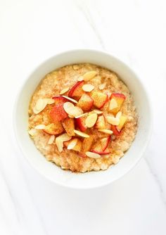 a bowl of oatmeal with apples and almonds in it on a white table