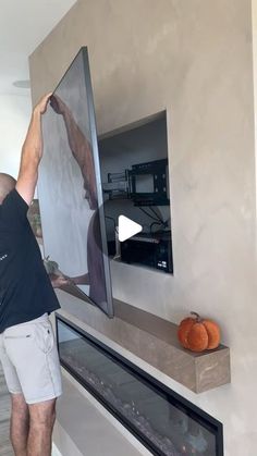 a man standing in front of a flat screen tv mounted on a wall next to a fireplace