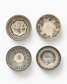 four bowls with designs on them sitting side by side in front of a white background