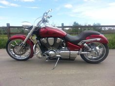 a red and black motorcycle parked on the side of a road next to a wooden fence