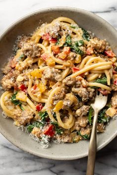 a bowl full of pasta with meat, spinach and cheese on it next to a fork