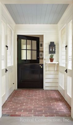 the front door is black and white with red brick flooring, an open shelf on the wall