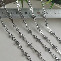 four silver chains on a table next to a measuring tape and potted plant in the background