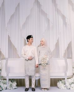 a man and woman standing next to each other in front of a white bench with flowers