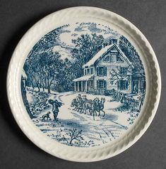 a blue and white plate with a horse drawn carriage in front of a country house