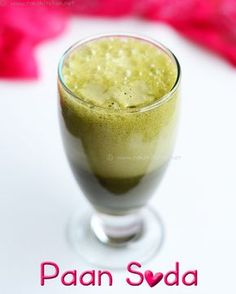 a glass filled with green liquid sitting on top of a white table next to pink flowers