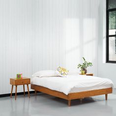 a bed sitting next to a window in a room with white walls and wooden furniture