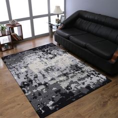 a living room with a black couch and white rug on the wooden floor next to a window