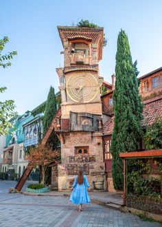 a woman in a blue dress walking past a tall tower with a clock on it