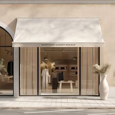 a store front with an open window and white vases on the sidewalk in front of it