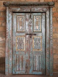 an old wooden door with decorative carvings on the front and side panels, against a brick wall