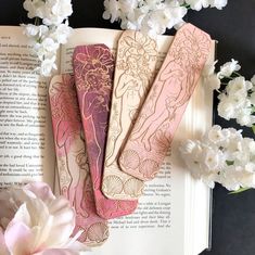 three bookmarks sitting on top of an open book next to flowers and white carnations