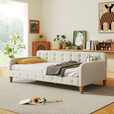 a white day bed sitting on top of a wooden floor next to a table with flowers