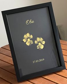 a black frame with yellow flowers on it sitting on a wooden table next to a white wall