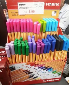 several different colored pens are on display in a box at a store with people behind them