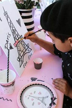 a young boy is painting the eiffel tower on a canvas at a table