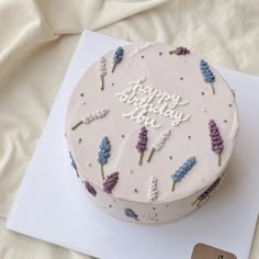 a white cake with purple flowers on it sitting on top of a card and envelope