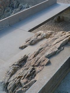 there are rocks and sand on the side of this concrete bench in front of a rock wall