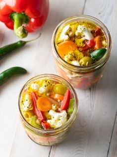 two jars filled with food sitting on top of a white wooden table next to green peppers