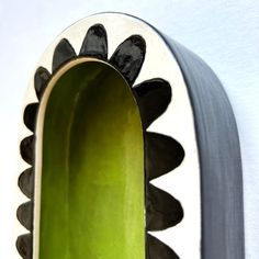 a green vase with black and white designs hanging from it's side on a wall