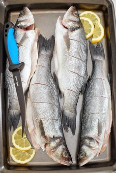 three fish in a pan with lemon slices and a knife