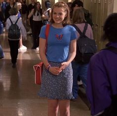 a woman in a blue shirt and floral skirt standing on a hallway with other people