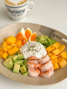 a plate with shrimp, avocado, and oranges on it next to a cup of coffee