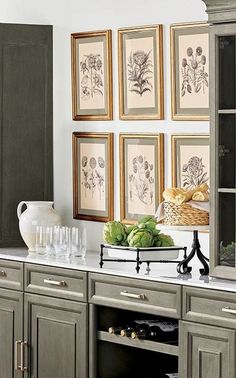 a kitchen with gray cabinets and pictures on the wall above it, along with wine glasses