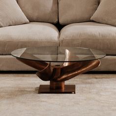 a glass table sitting on top of a wooden stand in front of a beige couch