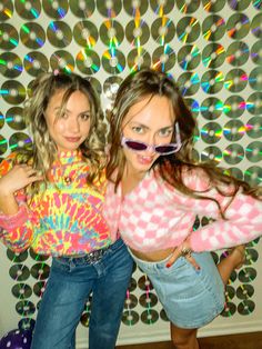 two young women posing for the camera in front of a wall with circles on it