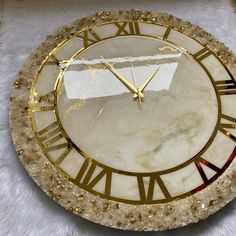 a clock that is sitting on top of a white surface with gold trim and roman numerals