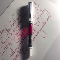 a fountain pen laying on top of a piece of paper with red ink and writing