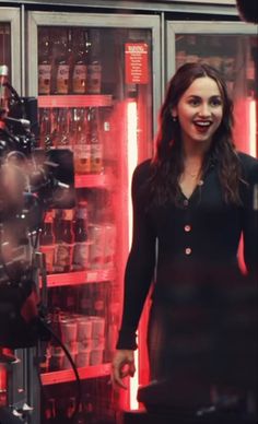 a woman is standing in front of a camera and some shelves full of beer bottles