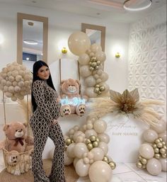 a woman standing next to balloons and teddy bears in a room filled with gold and white decorations