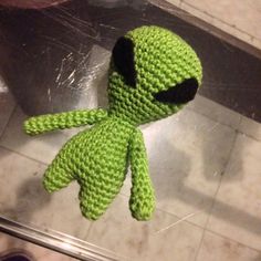 a green crocheted stuffed toy with black eyes and nose sitting on the floor