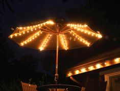 an umbrella with lights is lit up in the night sky over a table and chairs