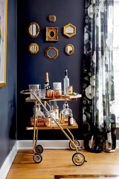 a bar cart with bottles and glasses on it in front of a wall decorated with mirrors