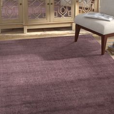 a living room area with a purple rug and white chair in front of a cabinet