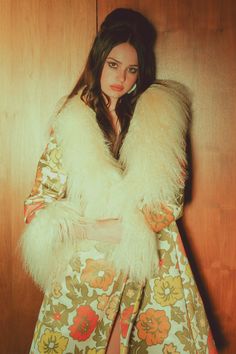 a woman in a floral dress and fur stoler posing for a photo with her hands on her hips