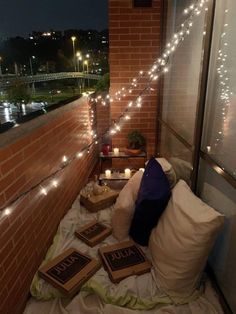 some lights are strung on the side of a brick building and there is a bed with pillows